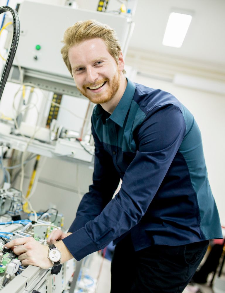 Man met rossig haar in een blauw overhemd, lachend en werkend aan een technisch apparaat in een industriële omgeving. Man met rossig haar in een blauw overhemd, lachend en werkend aan een technisch apparaat in een industriële omgeving.